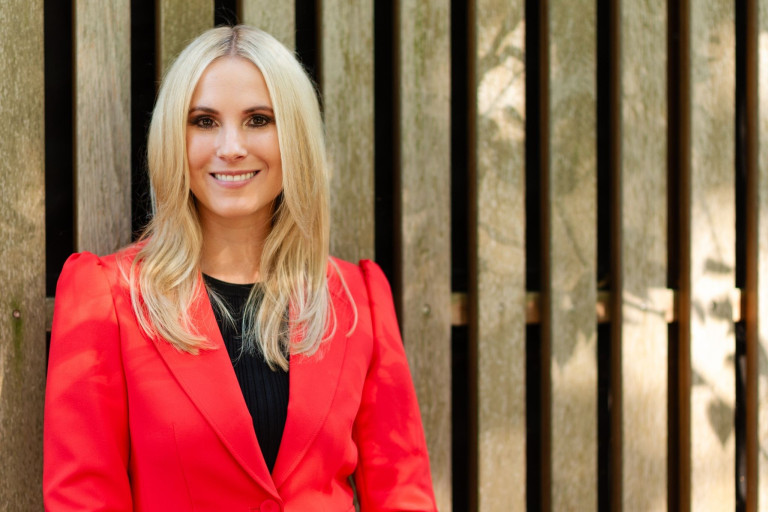 Frau im roten Blazer vor Holzwand als Symbolbild für Artikel über Lieblingsreiseziele