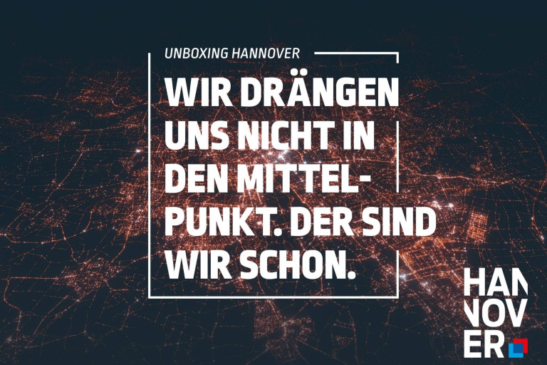 Unboxing Hannover: Zitat 'Wir drängen uns nicht in den Mittelpunkt. Der sind wir schon.' vor einer nächtlichen Stadtansicht von Hannover.