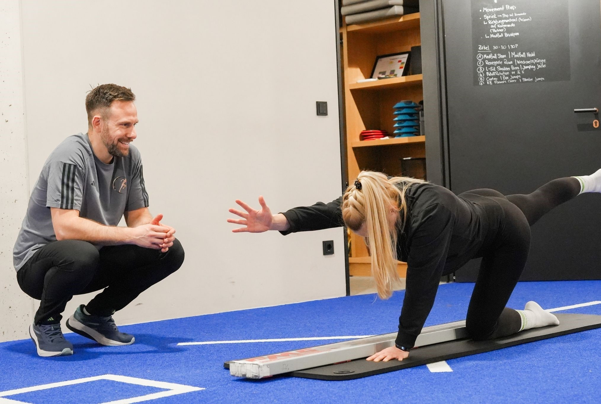 Laufteam beim Training in einem Fitnessstudio, Frau macht eine Übung auf blauer Matte
