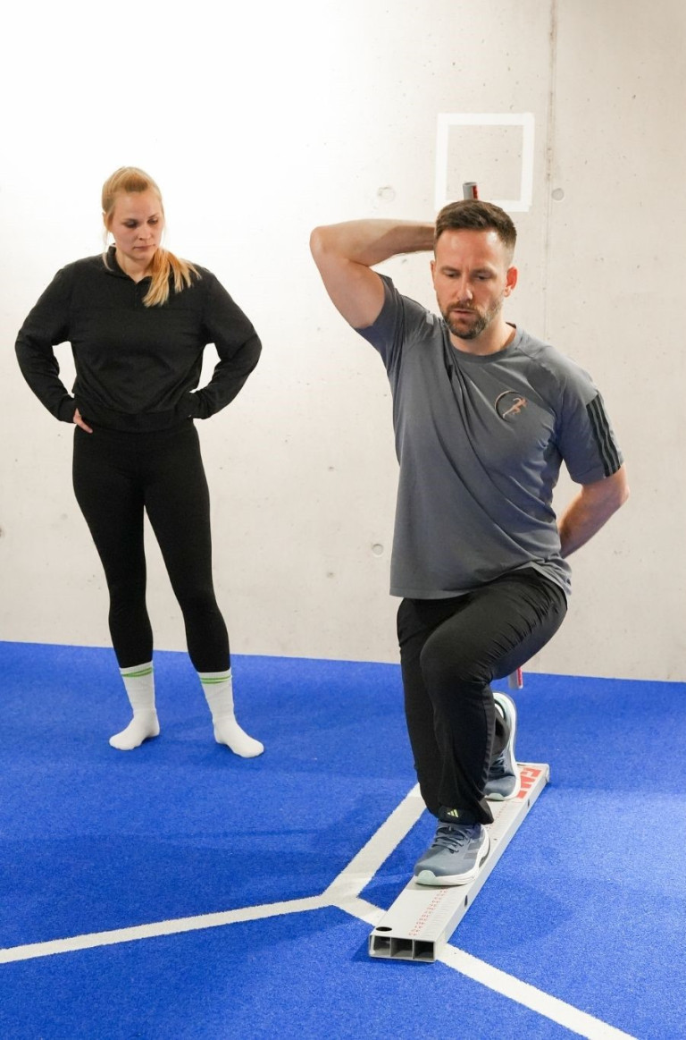 Laufteam Training: Fitnessübung und Betreuung auf blauer Matte Mitglieder eines Laufteams beim Training auf blauer Matte, eine Person macht eine Fitnessübung, die andere beobachtet.