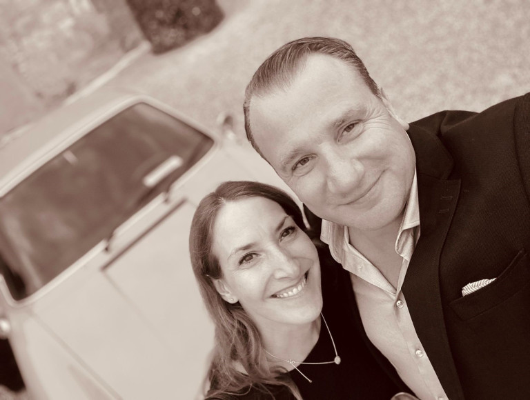 Hans Joachim Bischoff mit Begleitung vor einem klassischen Auto, sepiafarbenes Foto