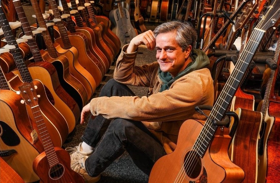 Person sitzt zwischen vielen Akustikgitarren in einem Musikgeschäft – Artikel Klang und Leben