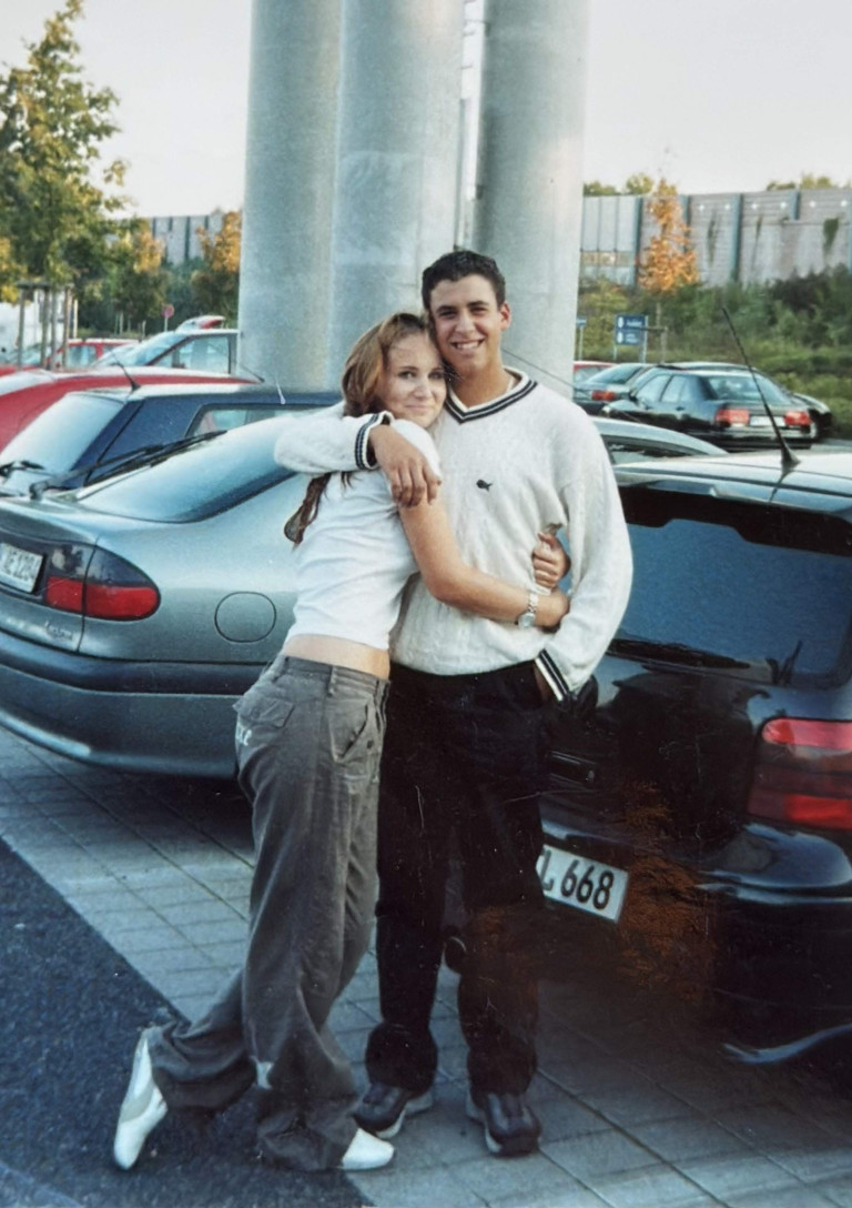 Junges Paar in den 90er Jahren umarmt sich auf einem Parkplatz, typische Mode der 90er