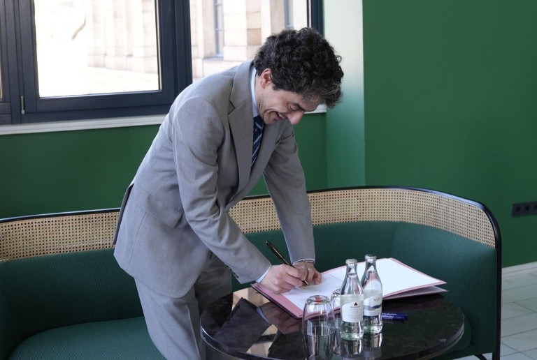 Musikdirektor beim Unterzeichnen eines Dokuments – Artikelbild Musikdirektor unterzeichnet Dokument am Tisch in modernem Büro