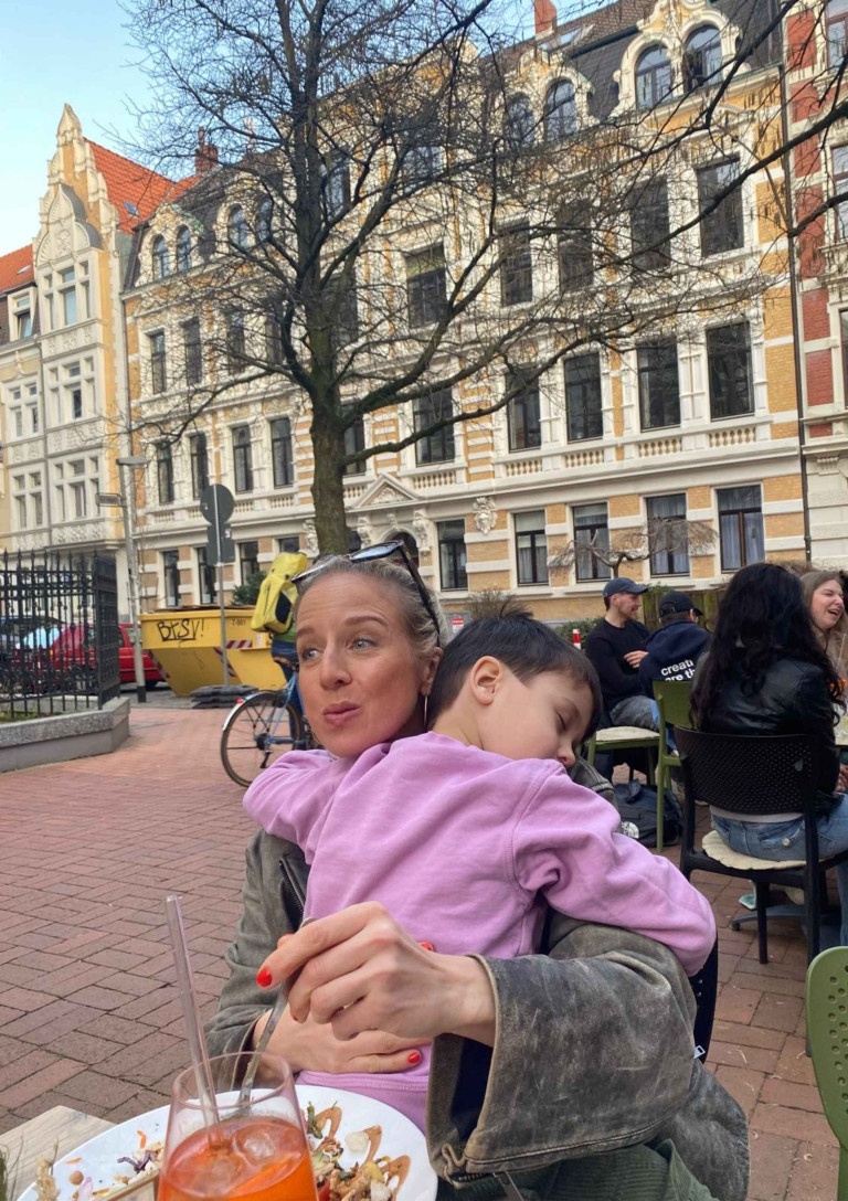 Lara Kertess mit Kind in einem Straßencafé vor historischer Häuserfassade