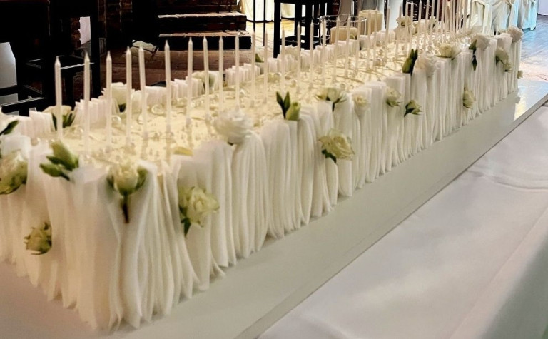 Festlich gedeckter Tisch mit weißen Servietten, Kerzen und Blumen bei Nobilis Event