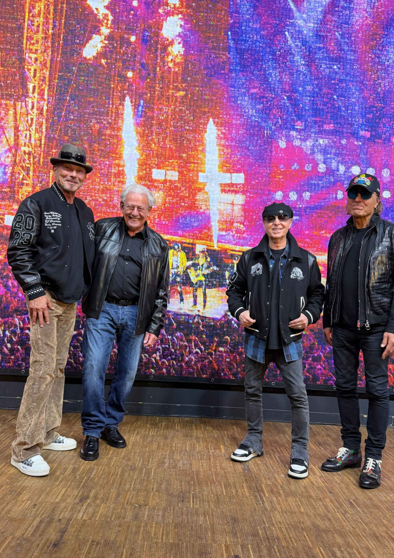 Pixel of Rock: Vier Männer posieren vor einer Rock-Mosaik-Wand Vier Männer in Rock-Outfits vor einer bunten Pixel-of-Rock-Mosaik-Wand