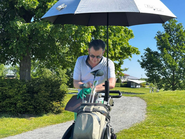 Person beim Golfen mit Schirm und Golftasche auf dem Golfplatz – bilder-nobilis-web