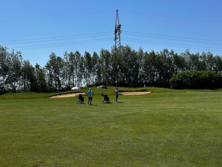 Golfer auf dem Nobilis Golfplatz bei sonnigem Wetter vor einem Sandbunker und Bäumen