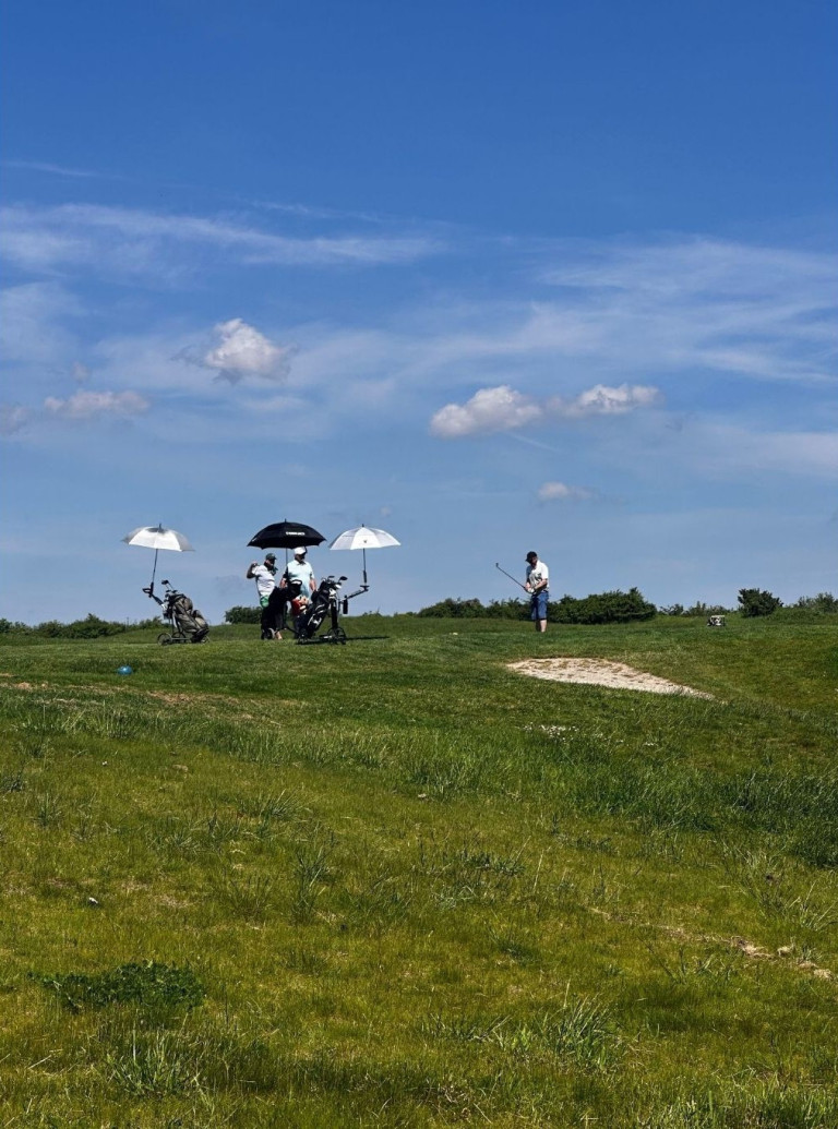 Golfspieler auf dem Nobilis Golfplatz bei sonnigem Wetter mit Schirmen und Golfausrüstung