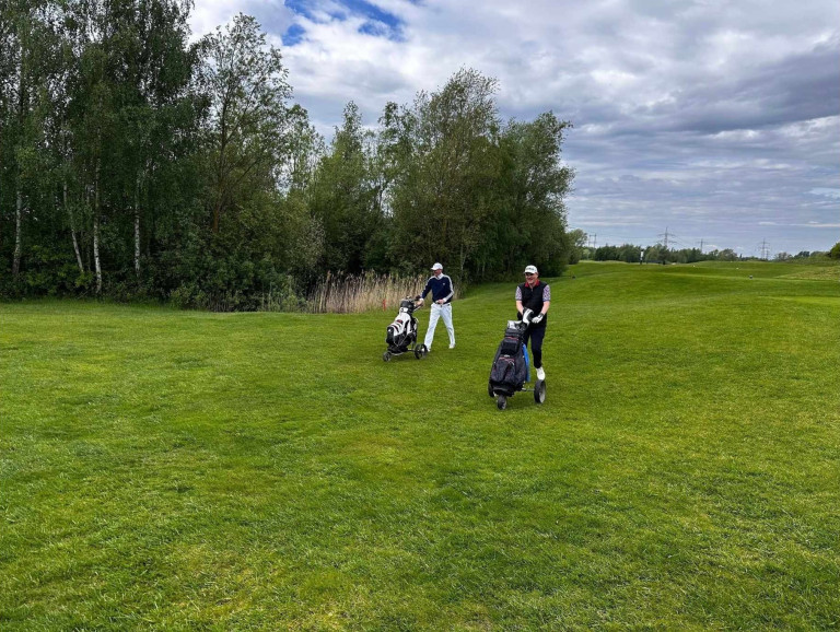 Zwei Golfer mit Trolleys auf einer grünen Wiese beim Golfplatz Nobilis
