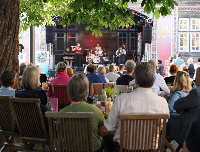 Kultursommer Open-Air-Konzert mit Livemusik und Publikum unter Bäumen Open-Air-Konzert beim Kultursommer, Publikum sitzt an Tischen unter Bäumen und genießt Livemusik auf der Bühne