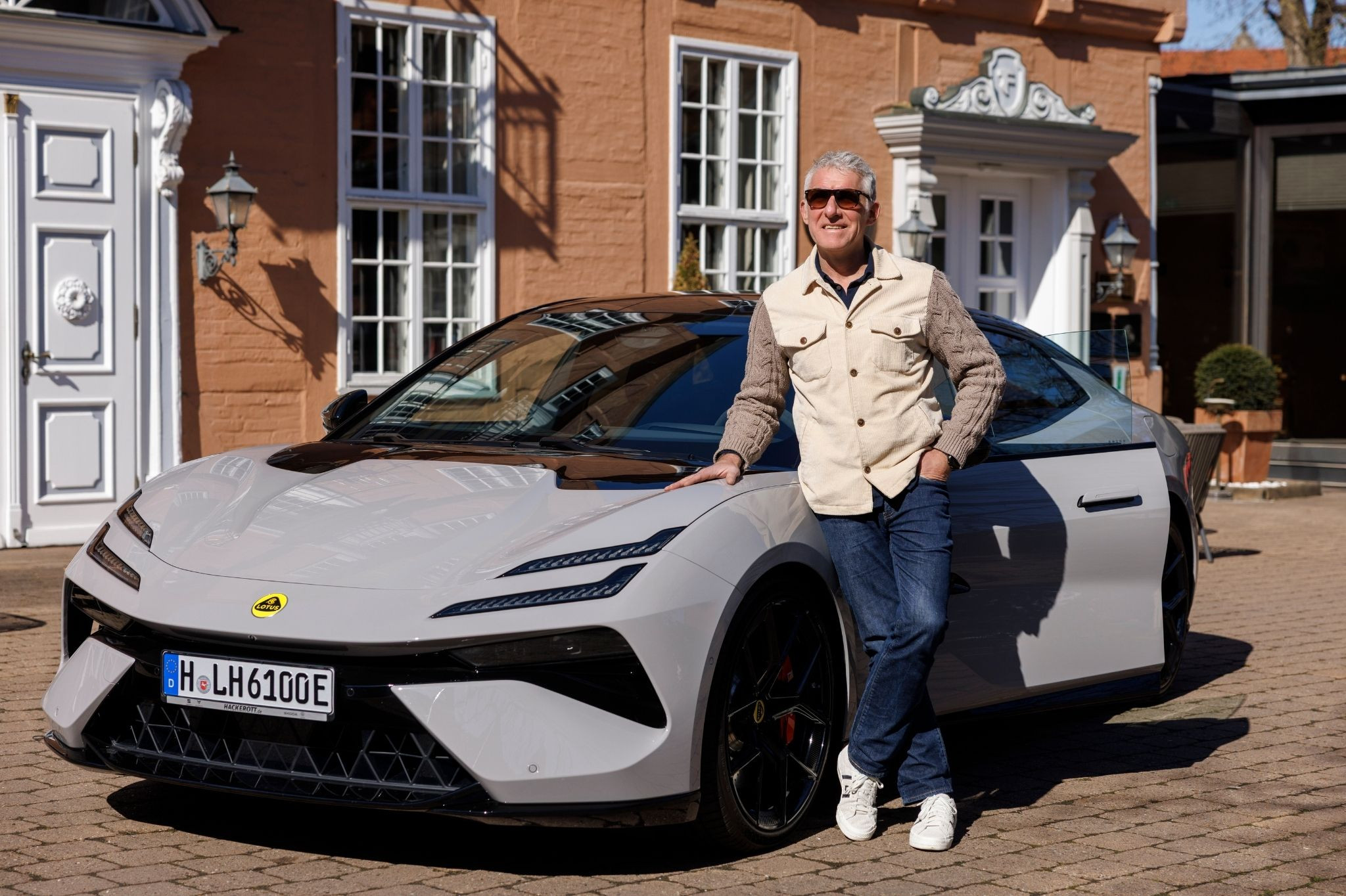 Person lehnt an einem weißen Lotus-Sportwagen vor einem Gebäude – artikel lotus mirko