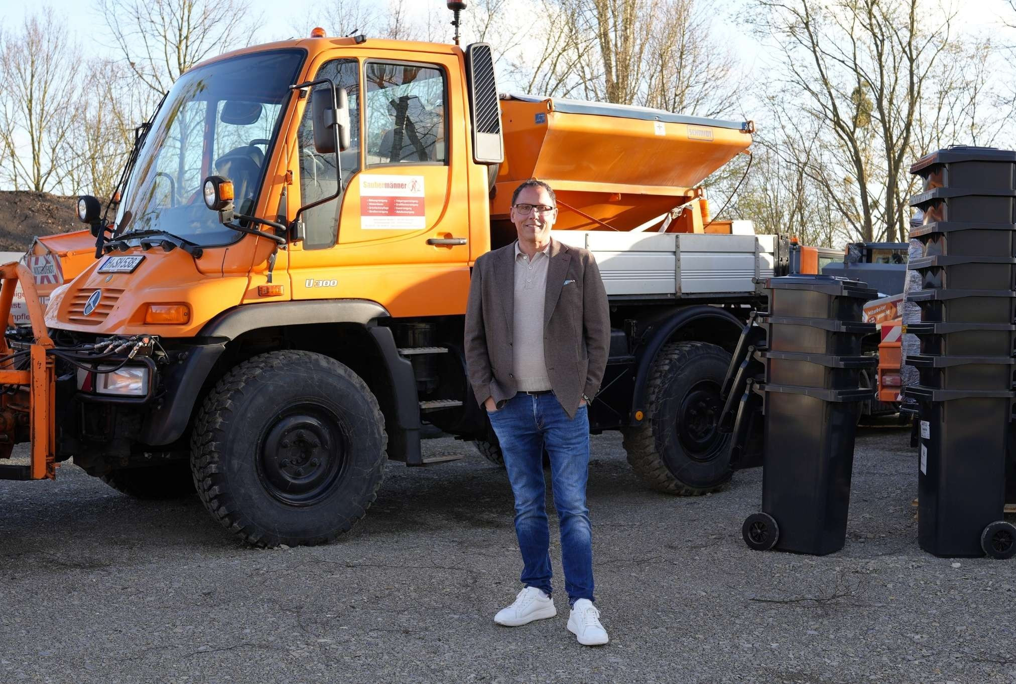 Michele Hust steht vor einem orangefarbenen Kommunalfahrzeug und Mülltonnen