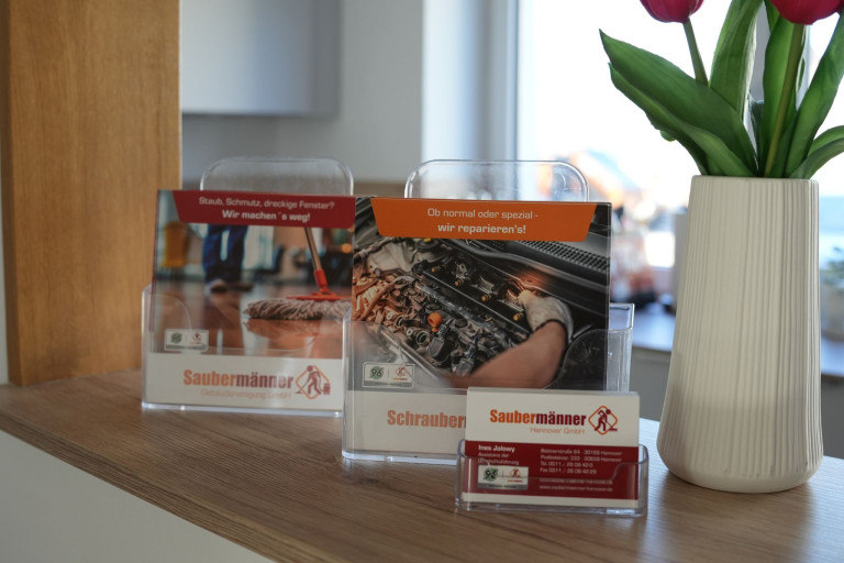 Flyer und Visitenkarte von Saubermänner Hannover GmbH – Gebäudereinigung und Reparaturservice Flyer und Visitenkarte der Saubermänner Hannover GmbH auf einem Tresen, mit Fokus auf Gebäudereinigung und Reparaturservice