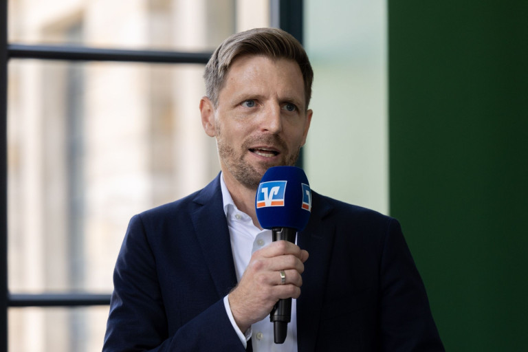 Mann im Anzug mit VR-Mikrofon bei einem Interview oder Vortrag, jw-19