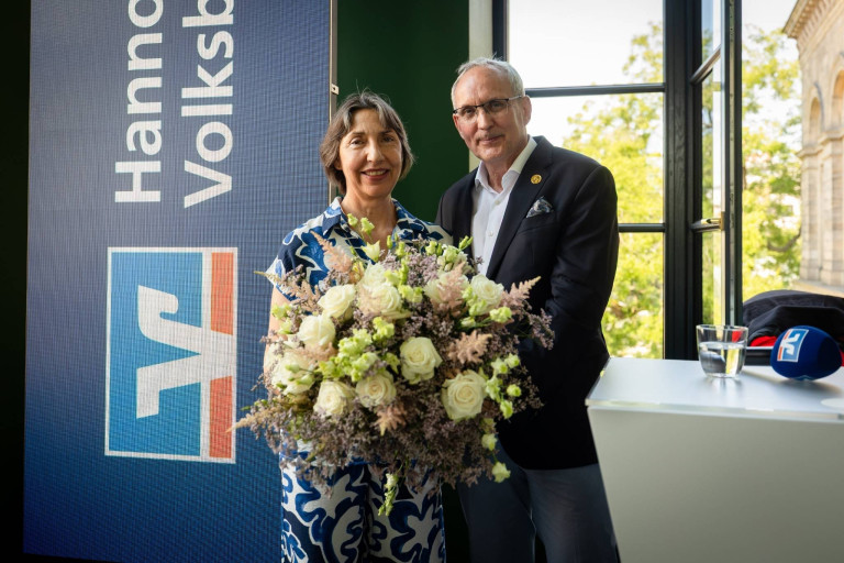 Zwei Personen mit großem Blumenstrauß bei Veranstaltung der Volksbank, Innenaufnahme mit Banner im Hintergrund