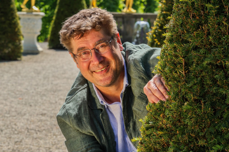 Desimo im Garten – Porträtfoto mit Hecke Desimo lächelt im Garten und lehnt an einer Hecke