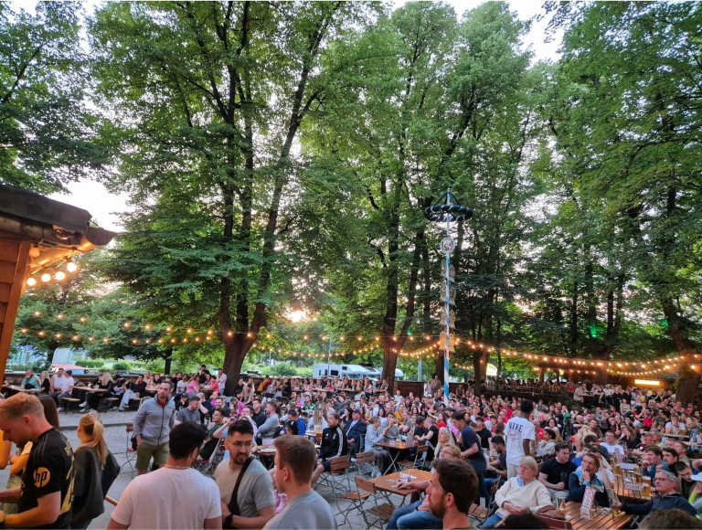 Großer Biergarten mit vielen Menschen bei einer Veranstaltung, abends unter Bäumen mit Lichterketten, bilder nobilis web