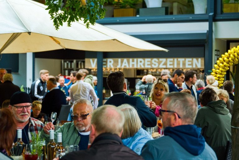 Menschen genießen eine Veranstaltung im Außenbereich des Restaurants Vier Jahreszeiten, geselliges Beisammensein unter Sonnenschirmen