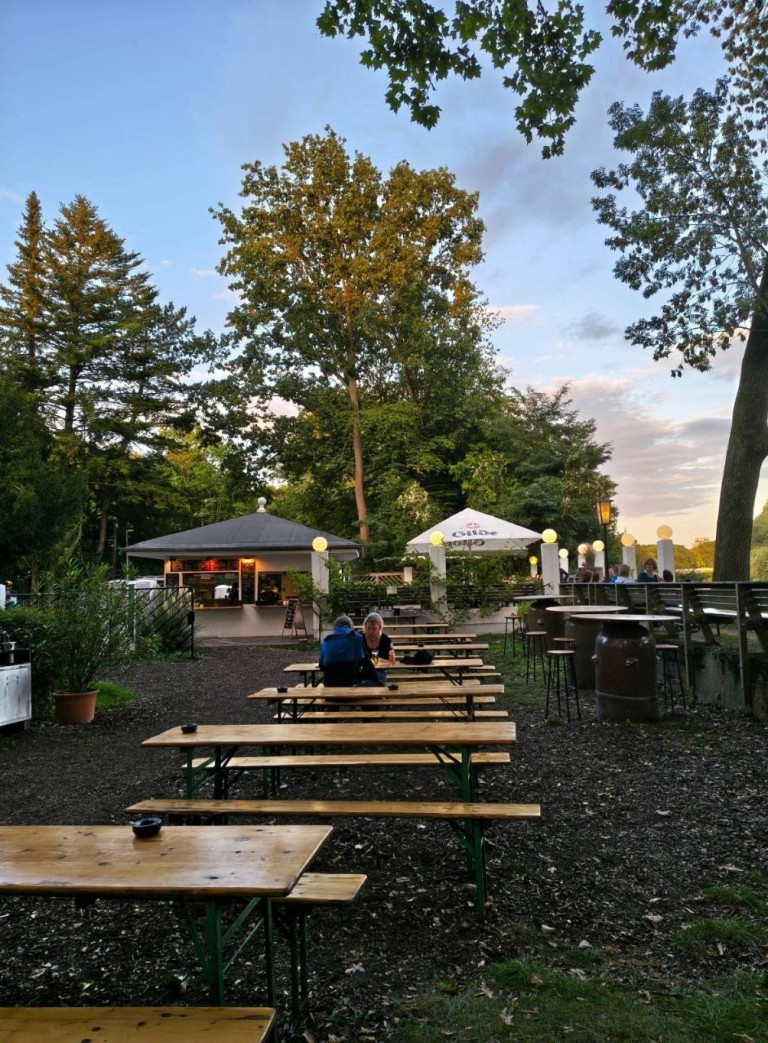 Biergarten mit Holzbänken und Bäumen bei Nobilis am Abend
