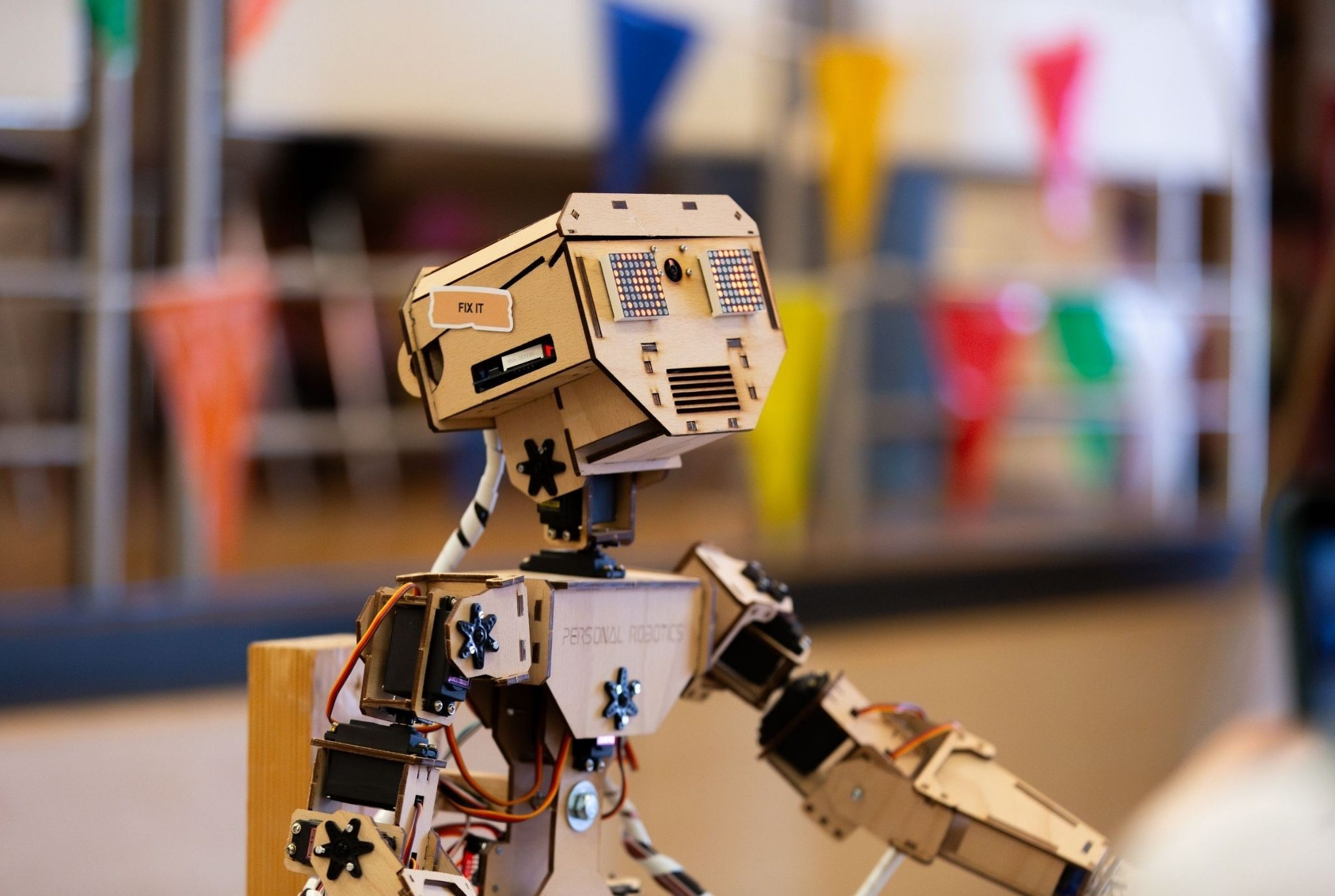 Holzroboter mit Schriftzug 'Personal Robotics' auf der Brust bei einer Veranstaltung, farbige Wimpel im Hintergrund