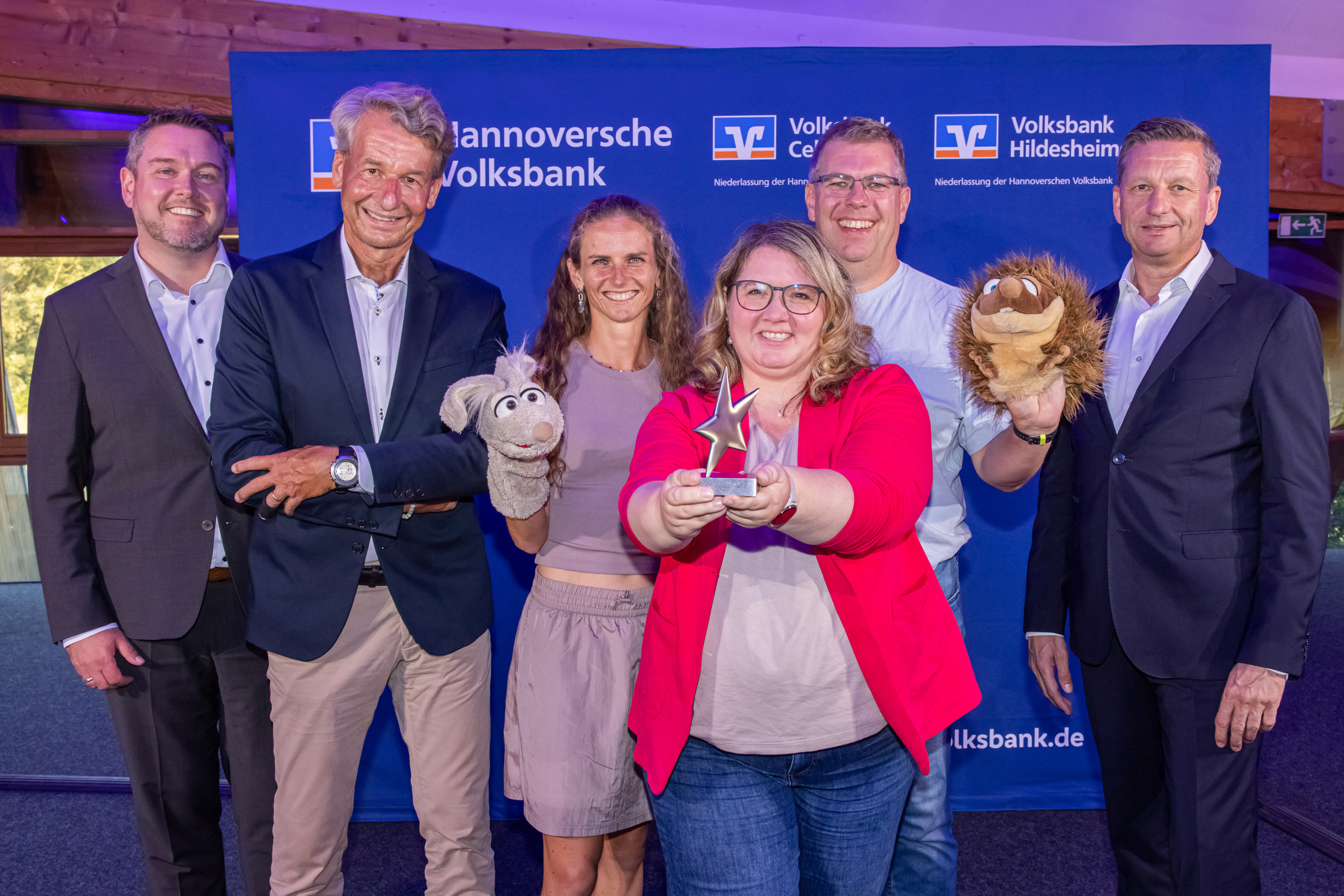 Gruppenfoto bei der Verleihung der Sterne des Sports mit Preisträgerin Herzig und Handpuppen vor dem Banner der Hannoverschen Volksbank und Volksbank Hildesheim