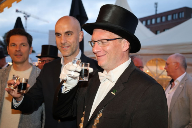 Festliche Veranstaltung mit Männern im Frack und Zylinder, Anstoßen mit Schnapsglas Zwei Männer auf einer festlichen Veranstaltung, einer trägt Frack und Zylinder und hält ein Schnapsglas