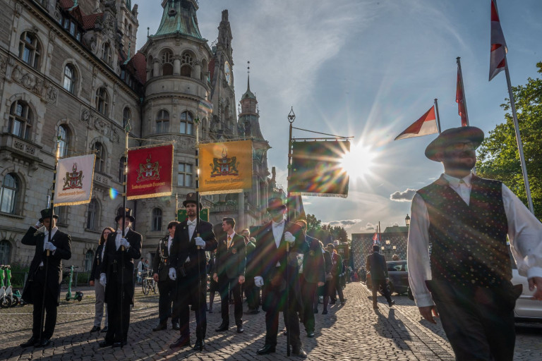 Traditioneller Festumzug mit Fahnen vor historischer Kulisse in Deutschland Traditioneller Festumzug vor historischem Gebäude mit Sonnenstrahlen und Fahnen in Deutschland