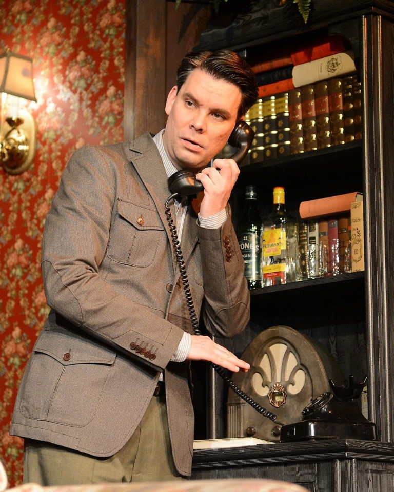 Schauspieler am Telefon im Nobilis Theaterstück vor Bücherregal – bilder-nobilis-web-5.jpg Schauspieler in klassischem Anzug telefoniert an einem alten Telefon vor Bücherregal – Szene aus Nobilis Theaterstück