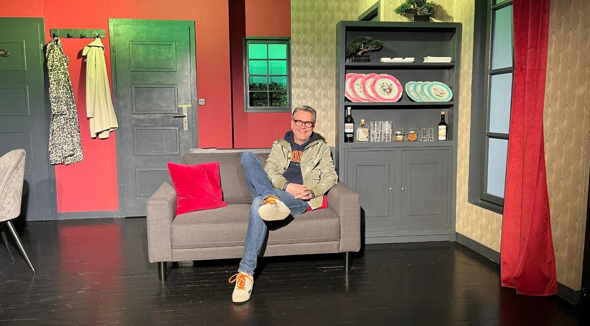 Mann sitzt entspannt auf grauem Sofa vor Regal mit Dekoration, Szene fr nobilis web