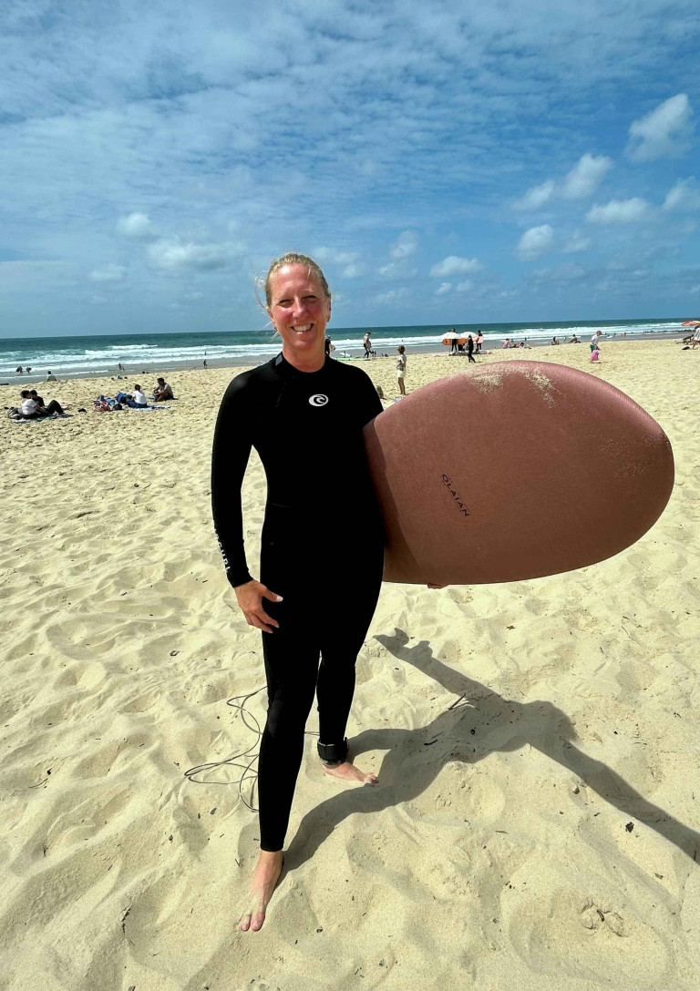 Surferin am Strand mit Surfbrett beim Sport Surferin mit Surfbrett am Sandstrand bei sonnigem Wetter