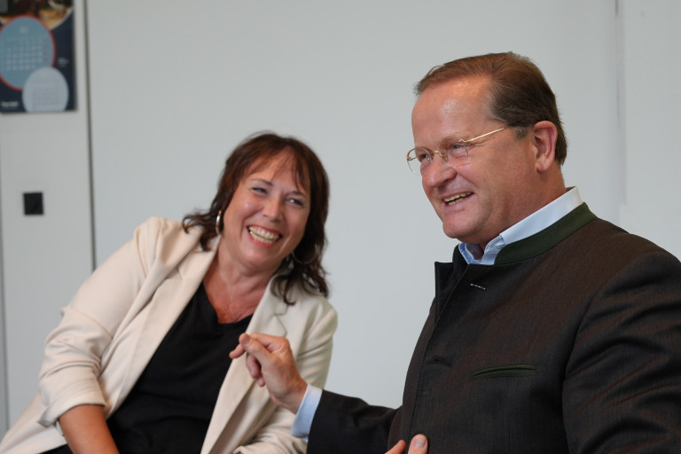 Programmleiterin Susanne Gruß und Schatzmeister Valentin Seidenfus haben Freude daran, Führungskräften neue Perspektiven aufzuzeigen. Zwei Menschen im Gespräch und lachend, freundliche Atmosphäre, Business-Meeting.