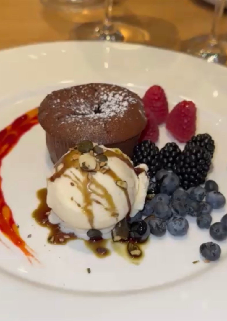Schokoladenkuchen mit Vanilleeis und Beeren als Dessert auf einem weißen Teller Schokoladenkuchen mit Vanilleeis, frischen Beeren und Saucen-Dekor auf einem weißen Teller