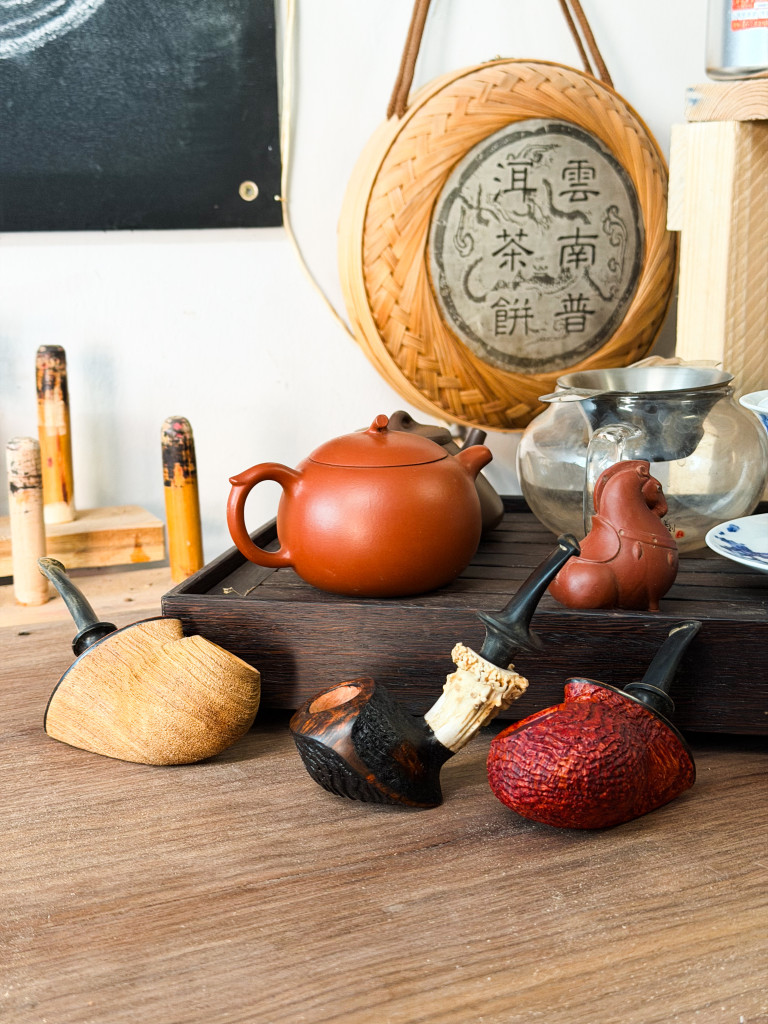 Verschiedene Tabakpfeifen und Teekanne auf einem Holztisch mit asiatischer Dekoration