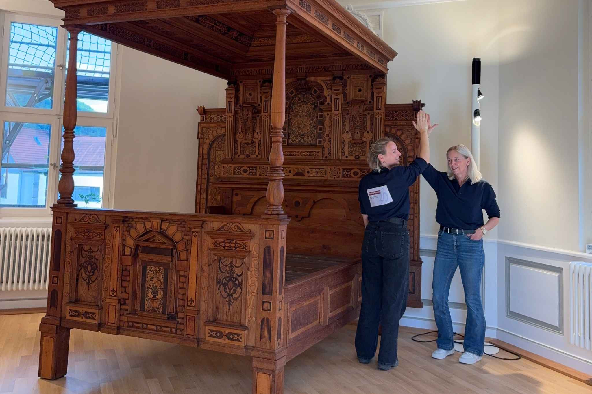 Barbara Helmrich vor einem kunstvoll verzierten historischen Bett in einem Ausstellungsraum