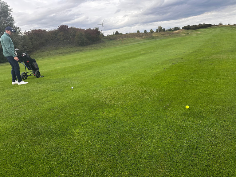Golfplatz mit Golfbällen und Windrad – nobilis Grasgeflüster Kolumne Rückenwind