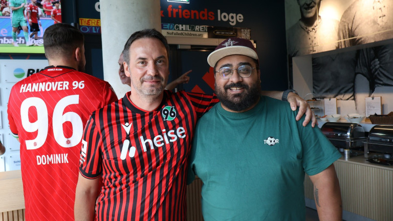 aptum and friends Loge bei Hannover 96 – Fans in der Loge mit Hannover 96 Trikot Zwei Männer in der aptum and friends Loge bei Hannover 96, einer trägt ein Hannover 96 Trikot, der andere ein grünes Shirt und eine Kappe.