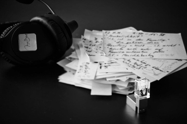 Audiograf mit Kopfhörer, handschriftlichen Notizen und USB-Stick auf schwarzem Hintergrund
