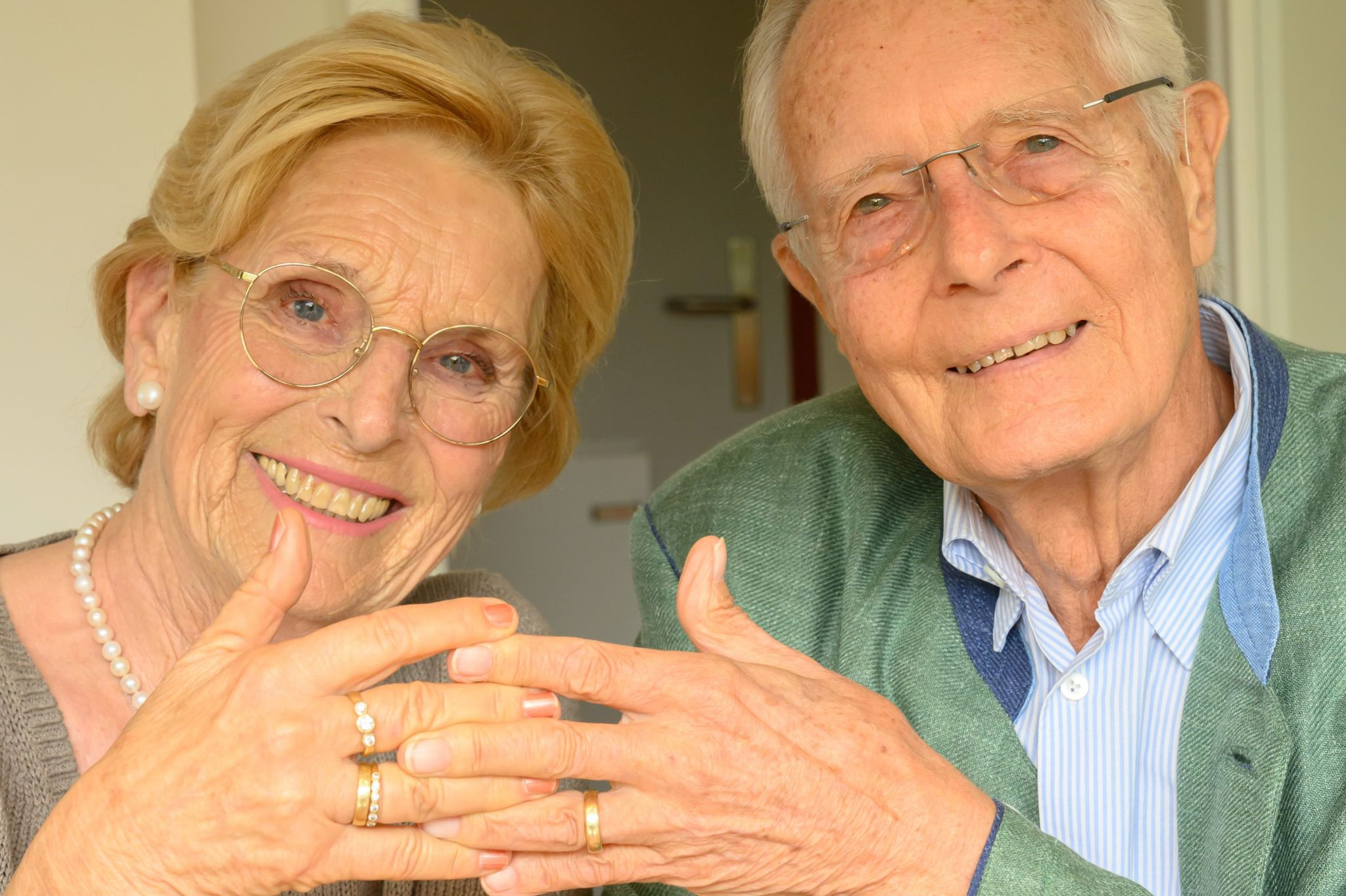 Lange Liebe: Älteres glückliches Paar zeigt Eheringe und lächelt in die Kamera