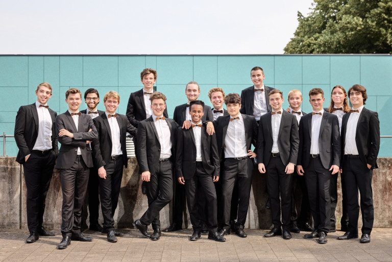 Gruppenfoto des Chores ffortissibros mit Oliver Borchert, alle Mitglieder in Anzügen vor moderner Wand