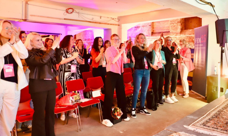 Gruppenfoto von applaudierenden Teilnehmerinnen bei einer Veranstaltung in Frankfurt am Main, modernes Ambiente mit roten Stühlen