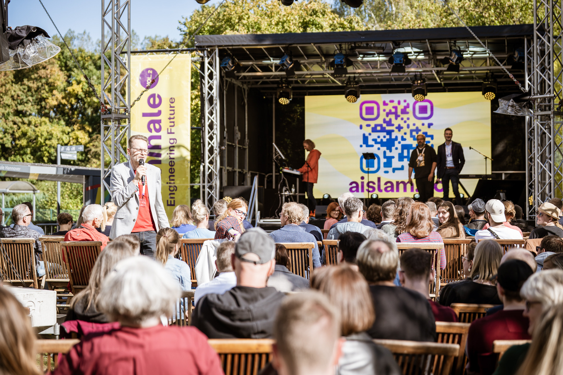Bühne mit Publikum beim liminale AI Slam 2, Open-Air-Event mit Vortrag und QR-Code auf Leinwand