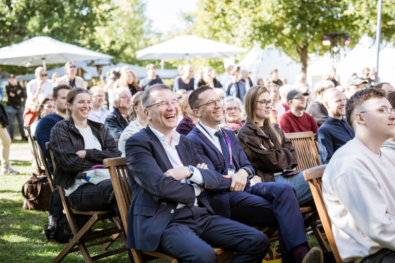 Liminale Atmosphäre – Falko Mohrs bei Outdoor-Veranstaltung mit begeistertem Publikum Liminale Atmosphäre bei einer Veranstaltung mit Falko Mohrs im Freien, lachende und interessierte Gäste im Publikum