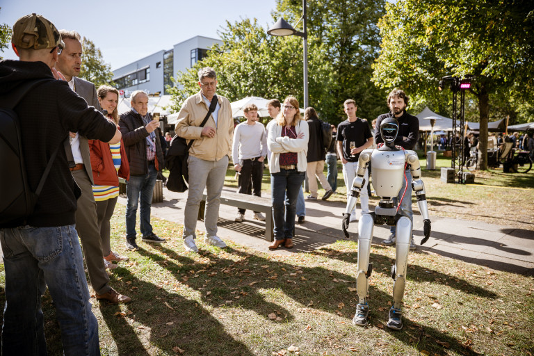 LIMINALE Atmosphäre – Thomas Seel und Besucher mit humanoidem Roboter auf Outdoor-Event LIMINALE Atmosphäre mit Thomas Seel: Menschen beobachten einen humanoiden Roboter im Freien
