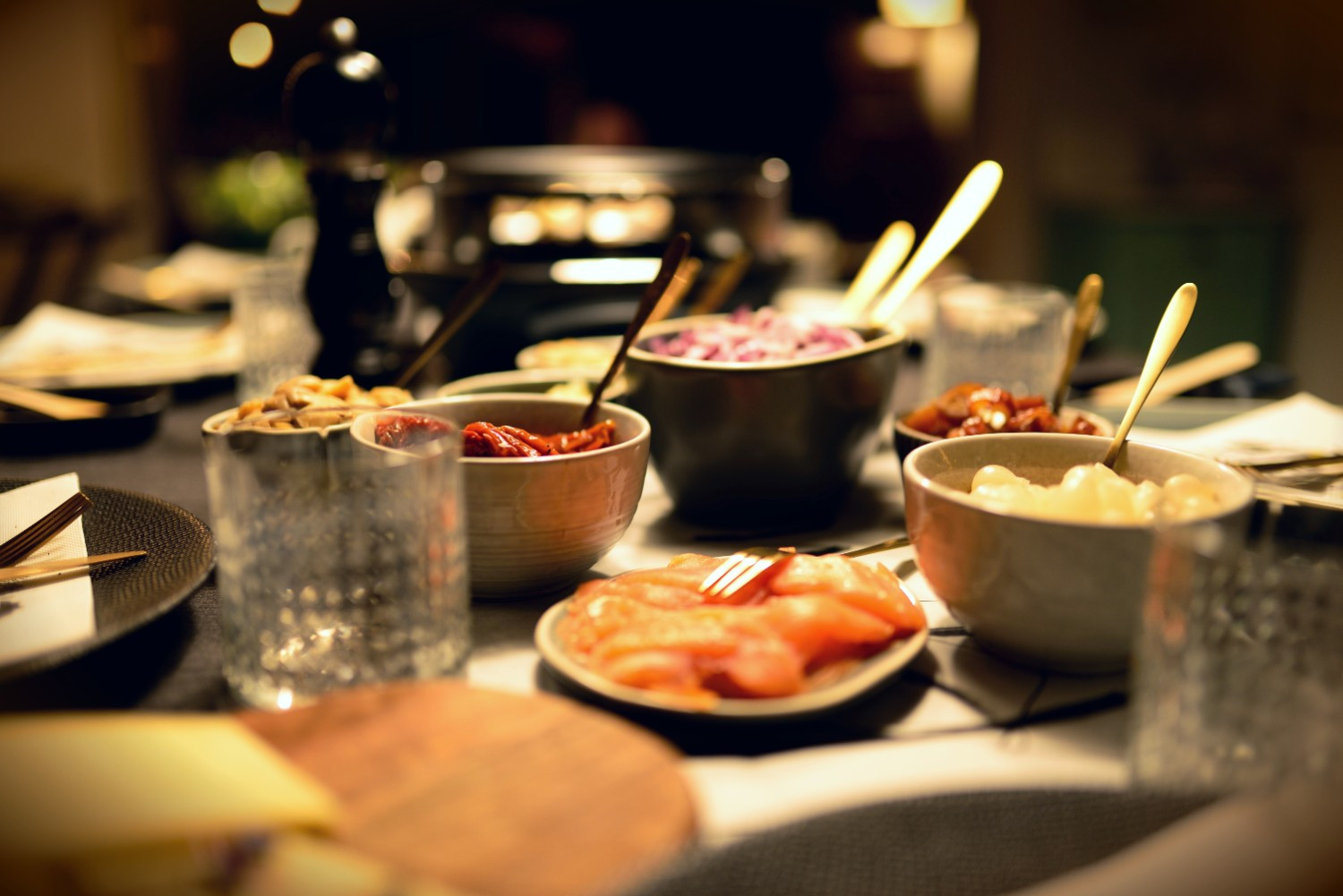 Raclette-Zutaten und Raclette-Grill auf einem festlich gedeckten Tisch, Foto von congerdesign