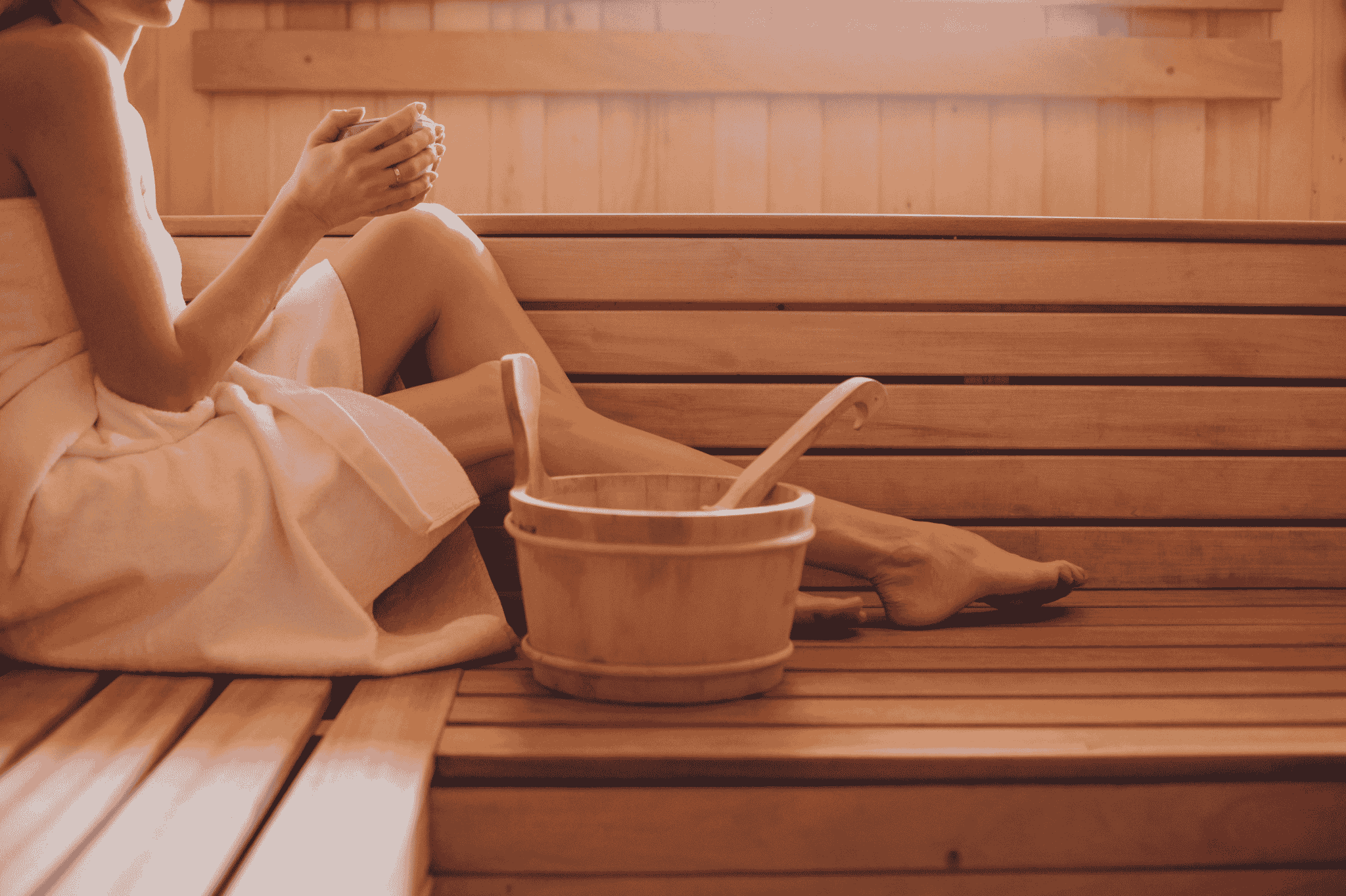Entspannte Person in der Sauna mit Handtuch und Aufgusskübel im Nobilis Web – Saunieren