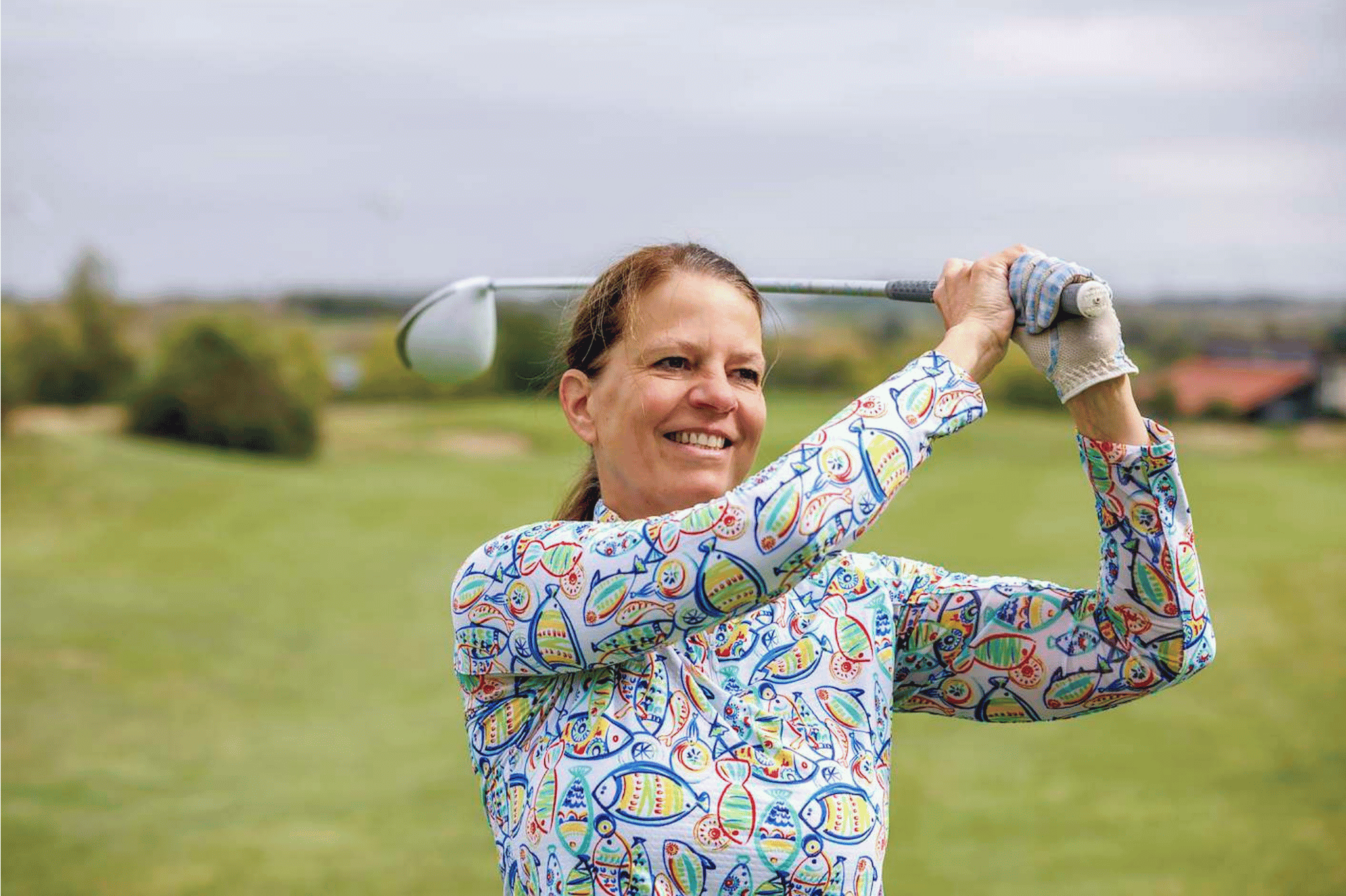 Frau spielt Golf auf dem Golfplatz, lächelnd nach dem Abschlag
