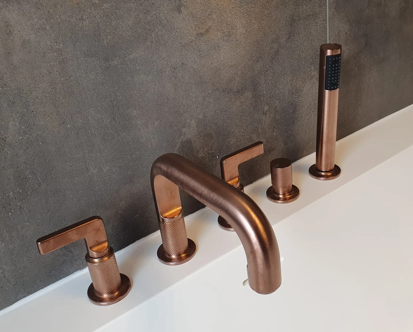 Moderne Badarmaturen in Kupferoptik auf weißer Badewanne vor grauer Wand