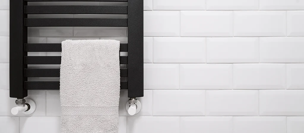 Moderner Badheizkörper mit Handtuch vor weißer Fliesenwand